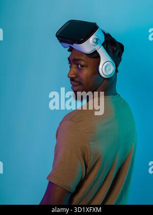 In a futuristic visual, an African American man stands isolated against a striking blue backdrop, adorned with VR glasses that t Stock Photo
