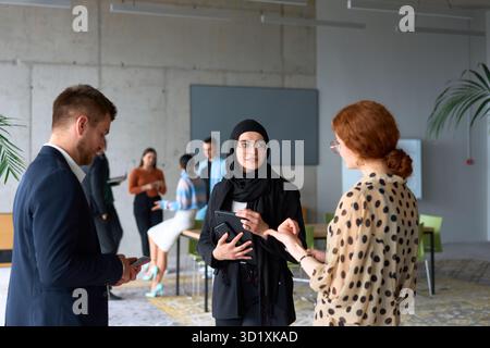 A diverse group of business professionals engages in a conversation during a work break in the office, with their colleagues vis Stock Photo