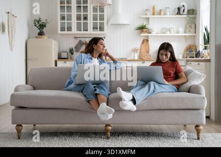 Family mother and daughter using laptops together while sitting on sofa in living room at home Stock Photo