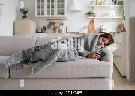Unhappy depressed teen girl lying on sofa using smartphone scrolling on social media. Cyberbullying Stock Photo