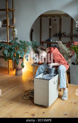 Craftswoman enjoying meditative process of making ceramics, shaping clay on pottery wheel Stock Photo