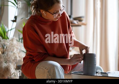 Focused craftswoman carefully shapes clay vessel spinning on potter wheel. Hobby concept Stock Photo