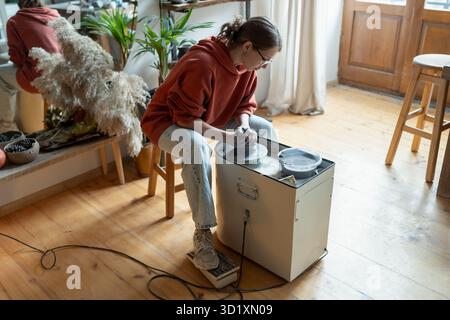 Concentrated craftswoman artist ceramist using potter wheel sits in studio to create clay sculpture Stock Photo