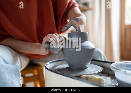 Creating clay formed ceramic art vase or pot on potter wheel in workshop for home improvement store. Stock Photo