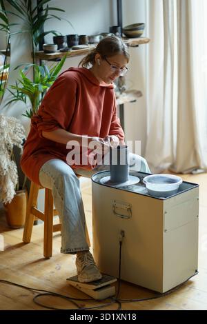 Focused artisan painstakingly working on manufacture of clay products on potters wheel in workshop. Stock Photo