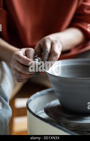 Female potter shaping wet clay on turning wheel into kitchenware in pottery studio Stock Photo