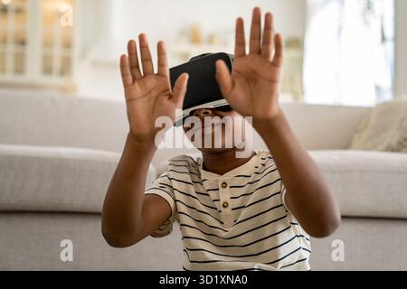 Small curious African American child boy wearing VR goggles spending time in virtual world Stock Photo