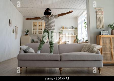 Carefree African boy child using VR helmet for fun and entertainment, flying in metaverse Stock Photo