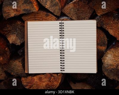 Open spiral notebook placed in center like a book on stacked firewood, warm matte tones, blank lined pages, soft firelight, cozy workspace, creative i Stock Photo