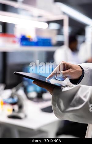 Close up of tablet running on advanced research in laboratory workspace, featuring data analysis and biotechnology equipment. Innovation lab for medical research and genetics. Stock Photo