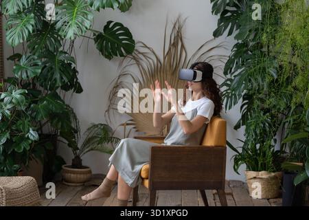 Young excited woman wearing VR glasses buying garden tools for home gardening in virtual reality Stock Photo