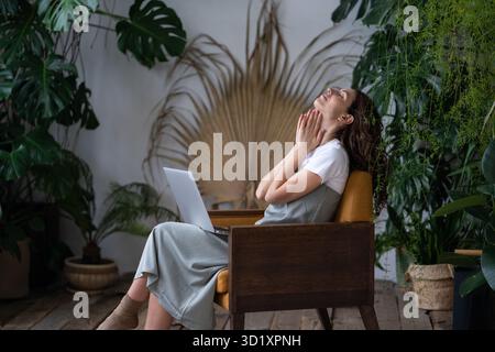 Thoughtful woman with closed eyes sitting on armchair after finishing work on project in homegarden. Stock Photo