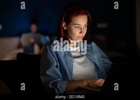 Woman uses laptop, works, studies. Overwork until late in evening, fatigue, hard study Stock Photo