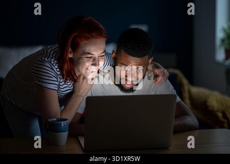 Happy romantic couple watching videos on Internet from laptop laugh smile enjoy funny comedy movie Stock Photo