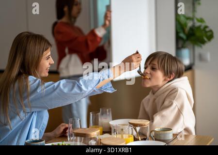 Happy mother feeding child son and smiling, mom and kid having fun while having breakfast together Stock Photo