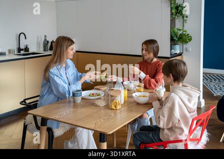 Family breakfast on kitchen, mom son daughter sitting at table eating together in morning. Stock Photo