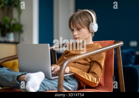 Schoolboy child in headphones studying online using laptop Stock Photo