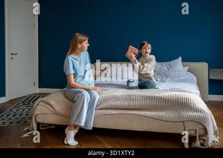 Excited kid shakes gift box near ear trying to guess what is inside, mom congratulating child boy. Stock Photo