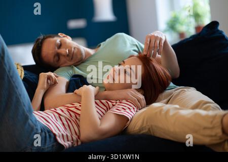Loving family couple relaxing lying on sofa at home. Well-rested wife and husband dreaming together Stock Photo