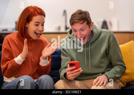 Excited overjoyed millennial happy young family couple looking at phone screen screaming with joy Stock Photo