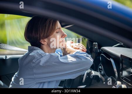 Pensive serious woman standing in traffic jam waiting driving car looking ahead. Stock Photo