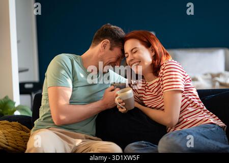 Happy carefree young couple in love joking laughing while relaxing on couch with coffee Stock Photo