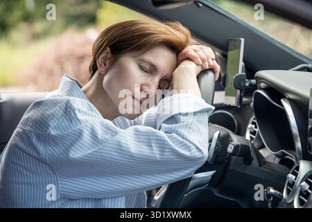 Middle aged tired woman sleeping on steering wheel exhausted from long driving in road trip. Stock Photo