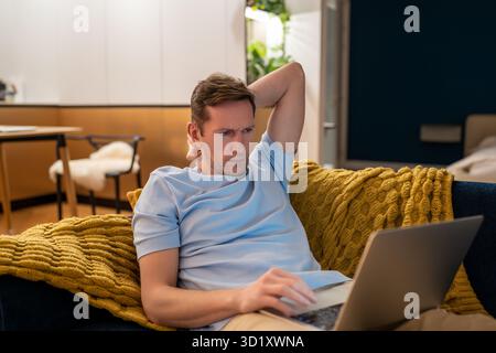Tired serious man working on laptop at home lying on couch, overworking, workaholic. Stock Photo