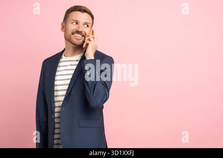 Confident businessman talking calling on smartphone looking aside on studio pink background. Stock Photo