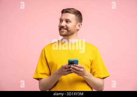 Happy cheerful guy holding smartphone interested looking away standing aside empty blank studio wall Stock Photo