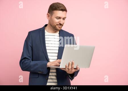 Pensive businessman with laptop isolated on pink wall working, types, chatting about work, business Stock Photo