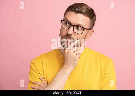 Thoughtful puzzled man thinks look away touching hand on chin ponder make decision over studio wall Stock Photo