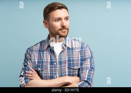 Contented satisfied guy smiles, looks away isolated background. Confident man crossed arms in studio Stock Photo
