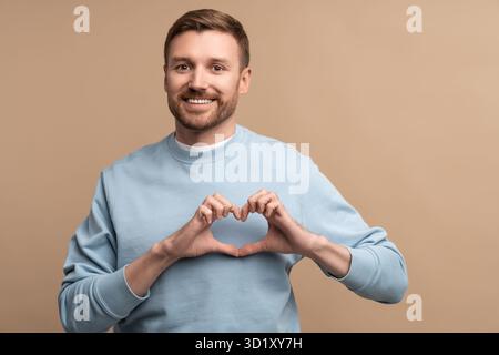 Feeling happy in love smiling man making sign heart shape look at camera isolated studio background Stock Photo