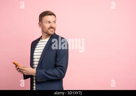 Businessman with smartphone isolated on pink background. Guy turns around, looks back with interest. Stock Photo