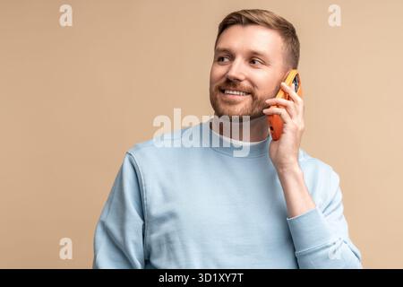 Happy smiling middle aged man talking calling phone on beige background looking aside. Stock Photo