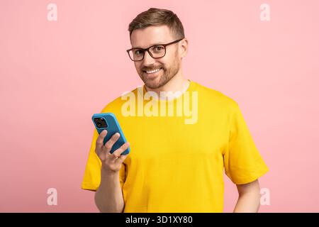 Satisfied with good news smiling bearded man in glasses looking at camera with mobile phone in hand Stock Photo