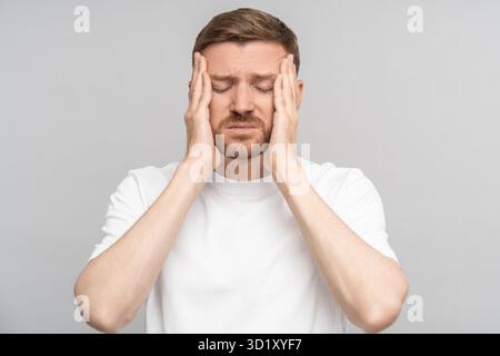 Tired man holds his head suffering from pain. Headache, migraine, overwork, illness, cold. Stock Photo