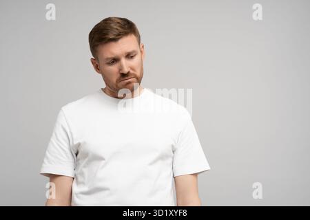 Sad disappointed man with head down on gray background. Portrait of young upset frustrated guy. Stock Photo