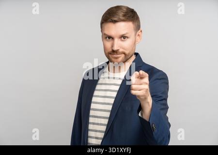 Portrait of confident bearded businessman pointing finger ahead looking at camera and smiling. Stock Photo