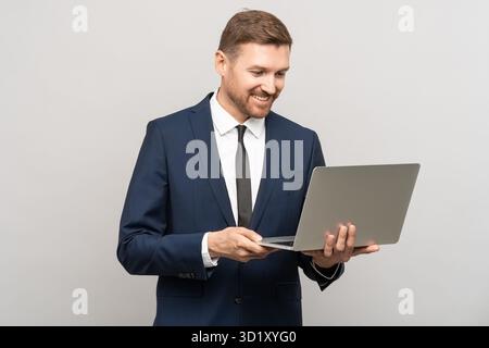 Pleased businessman looking at laptop screen smiling. Studio portrait isolated on gray background Stock Photo