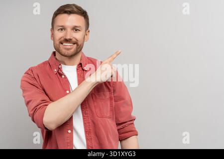 Amity smiling man pointing index finger by side on copy space for advertising on studio background. Stock Photo