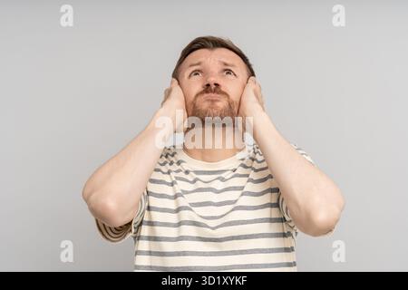 Man covers ears with hands looks up. Annoying noise loud sounds. Stressed by hum vociferous fight Stock Photo