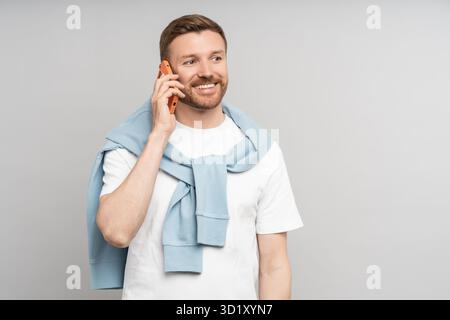Happy positive middle aged man talking on smartphone isolated on gray background. Stock Photo
