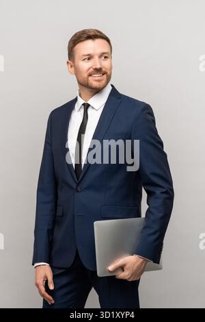 Successful male businessman confident look with laptop in hand standing isolated grey background. Stock Photo