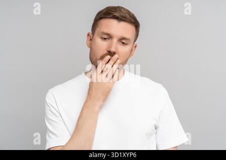 Sleepy yawning man with closed eyes opened mouth covering hand on gray background. Stock Photo