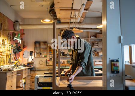 Concentrated carpenter working on making a table, using clamping brackets and bar clamps. Woodwork. Stock Photo