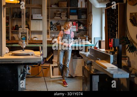 Peaceful artisan craftswoman at workplace in woodwork work shop. Pensive woman at creative studio. Stock Photo