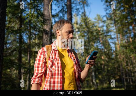 Man uses smartphone in woods looking for route through forest using map app. Hiker walking in nature Stock Photo