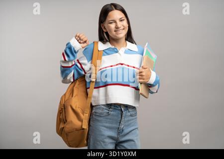 Positive student teen school girl rejoice on grey studio blank with backpack, education notebooks Stock Photo